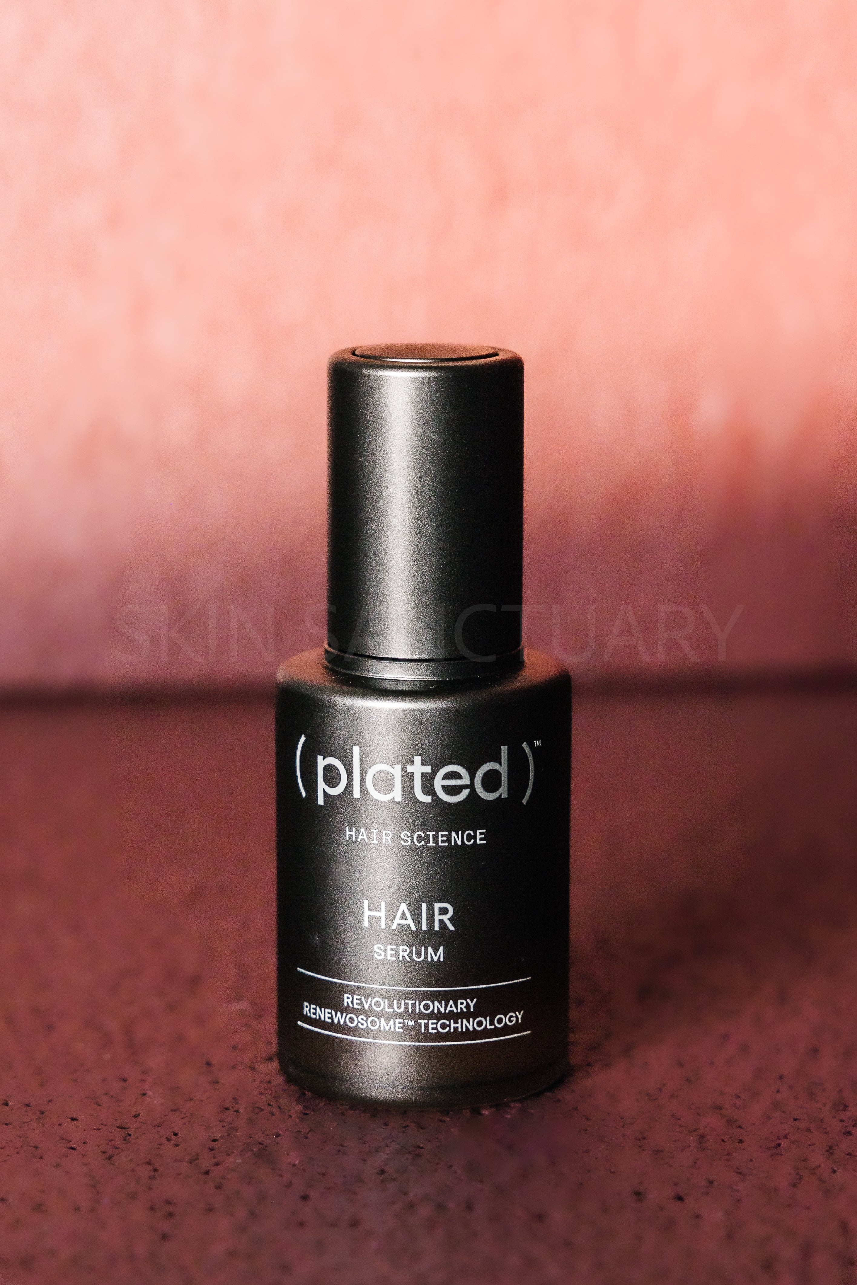 Black hair serum bottle labeled 'plated' on a textured surface with a blurred background.